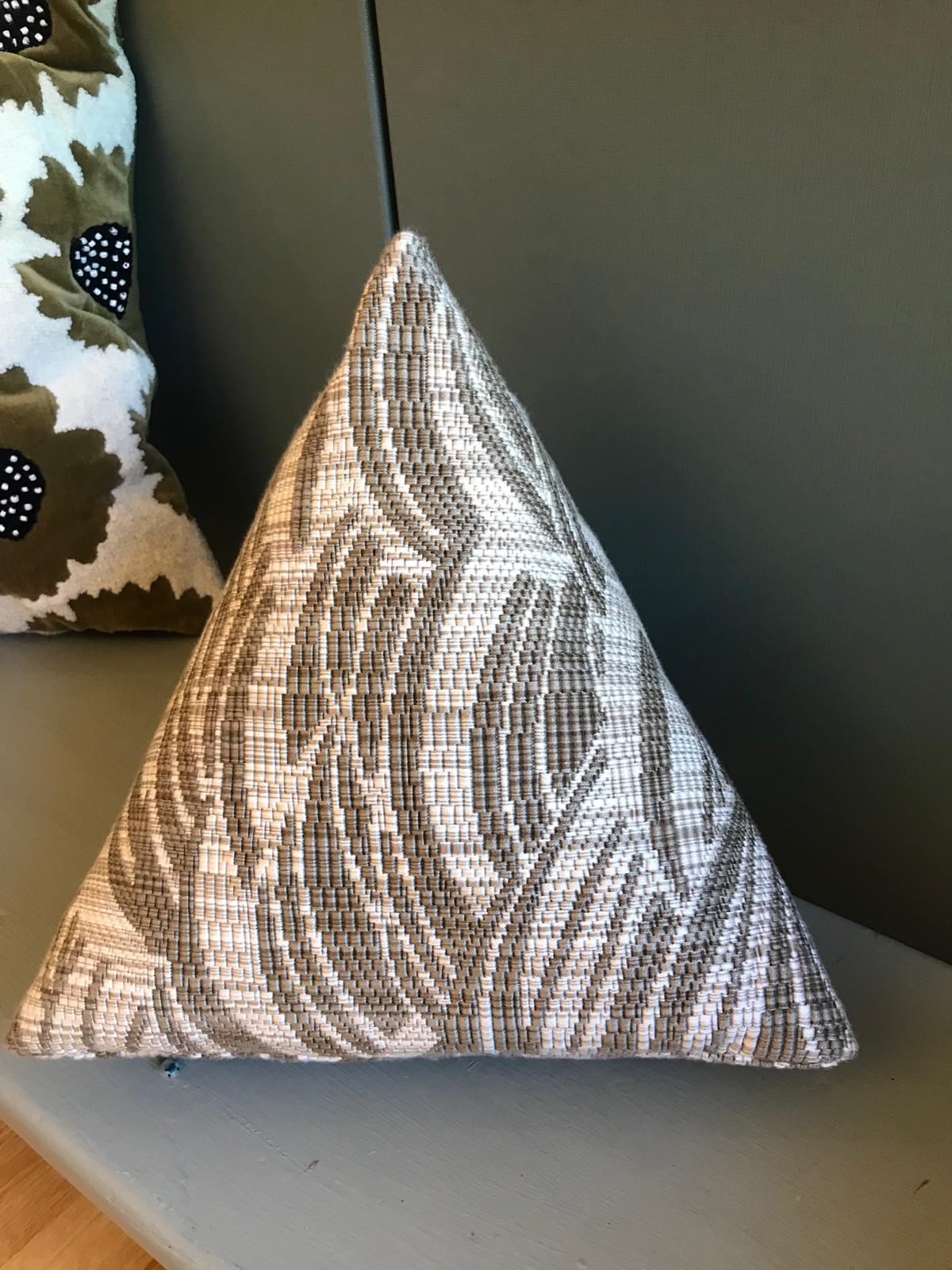 Coussin triangulaire beige à motif tissé géométrique devant un fond kaki