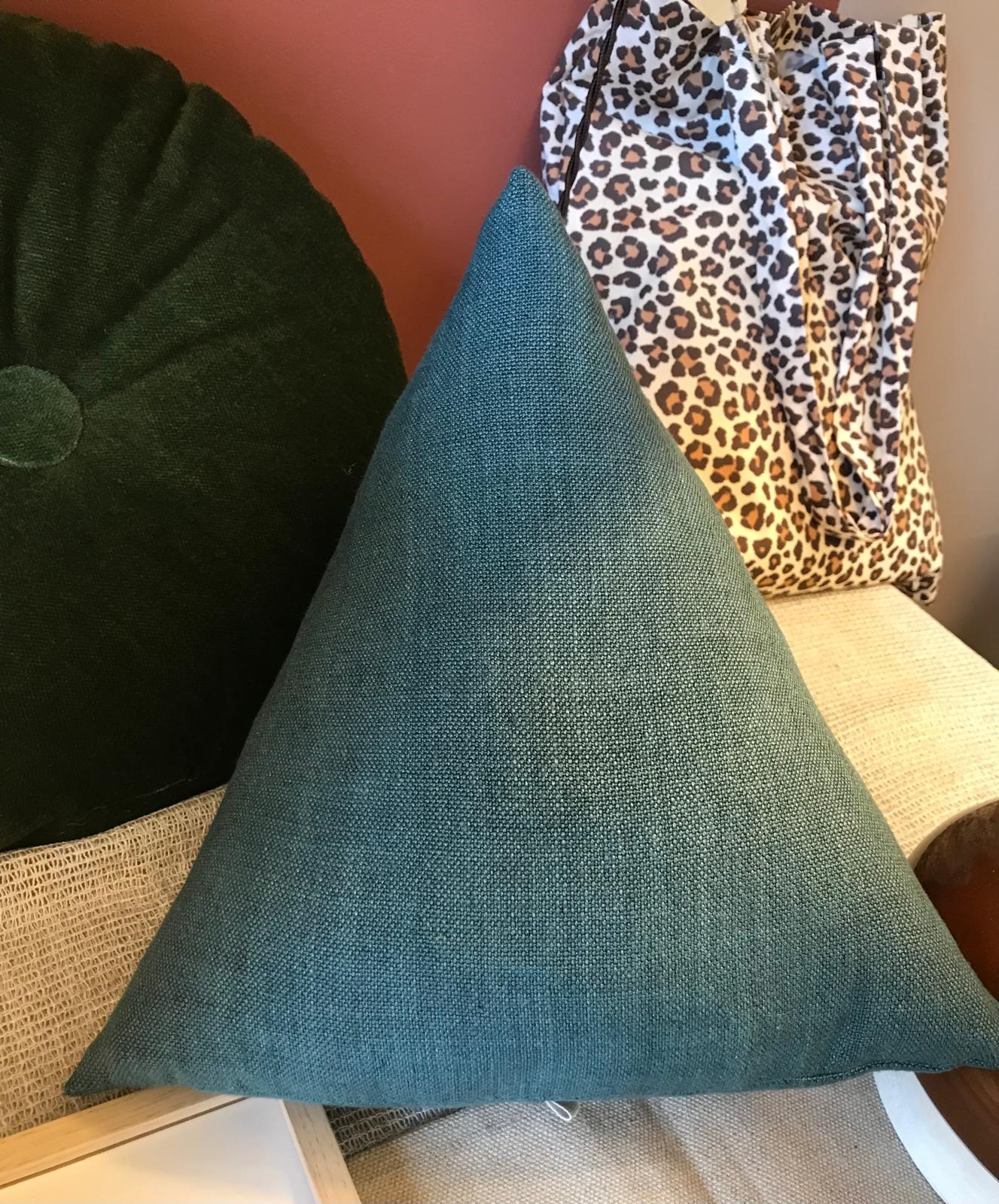Coussin triangulaire bleu canard devant un sac léopard
