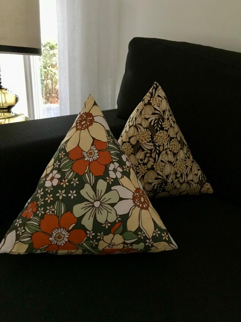 Deux coussins triangulaires fleuris posés sur un canapé noir