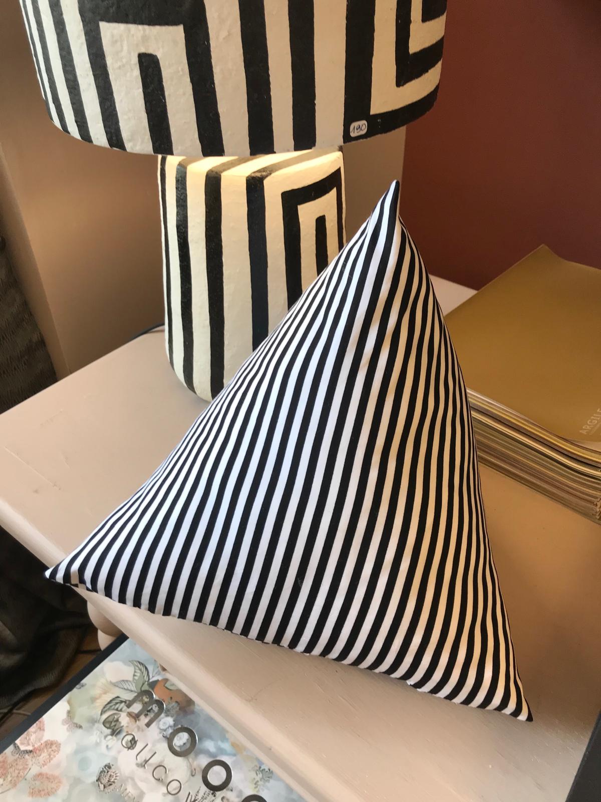 Coussin triangulaire rayé noir et blanc près d'un pied de lampe graphique