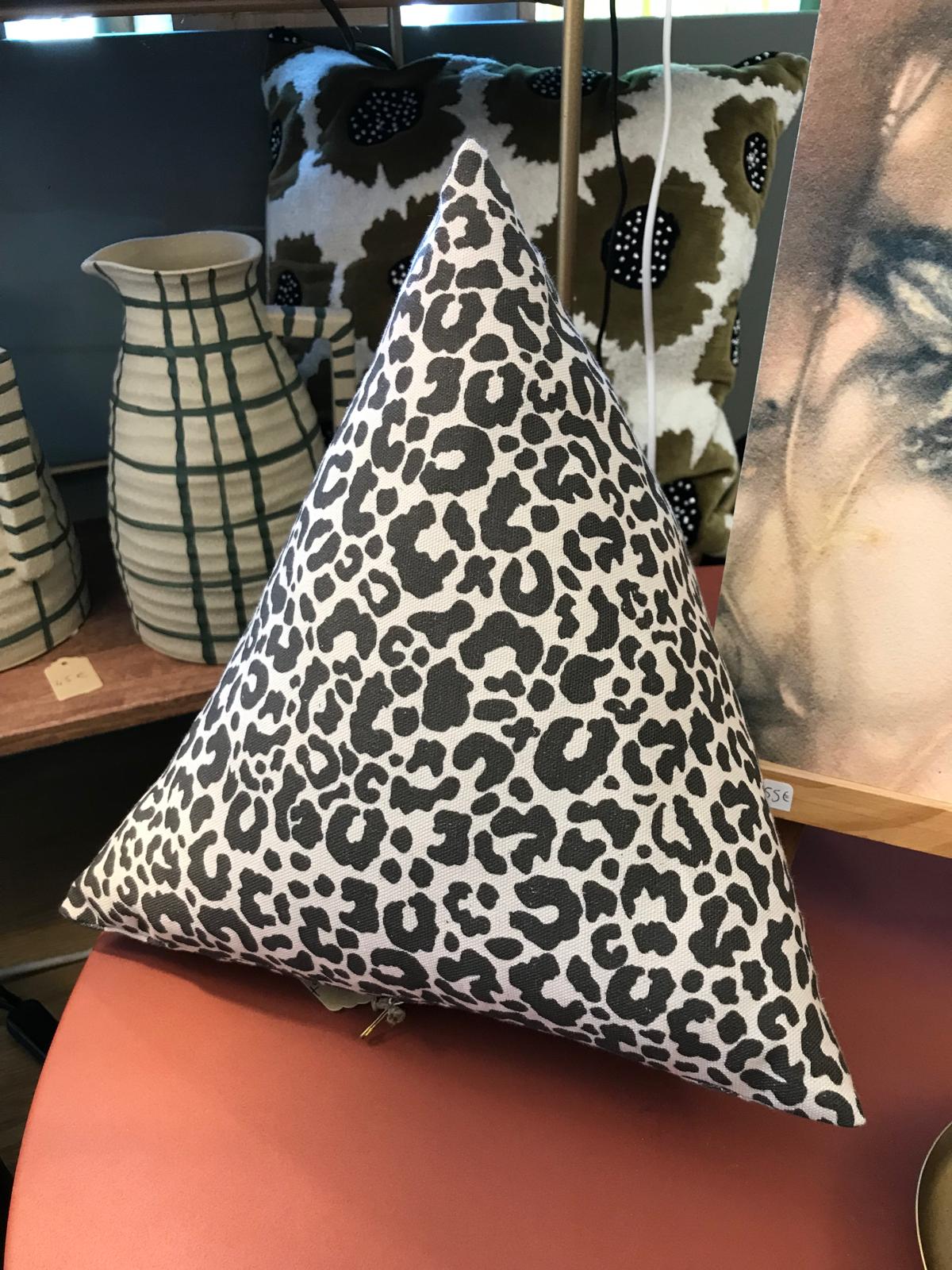 Coussin triangulaire léopard posé devant des vases et un grand coussin fleuri