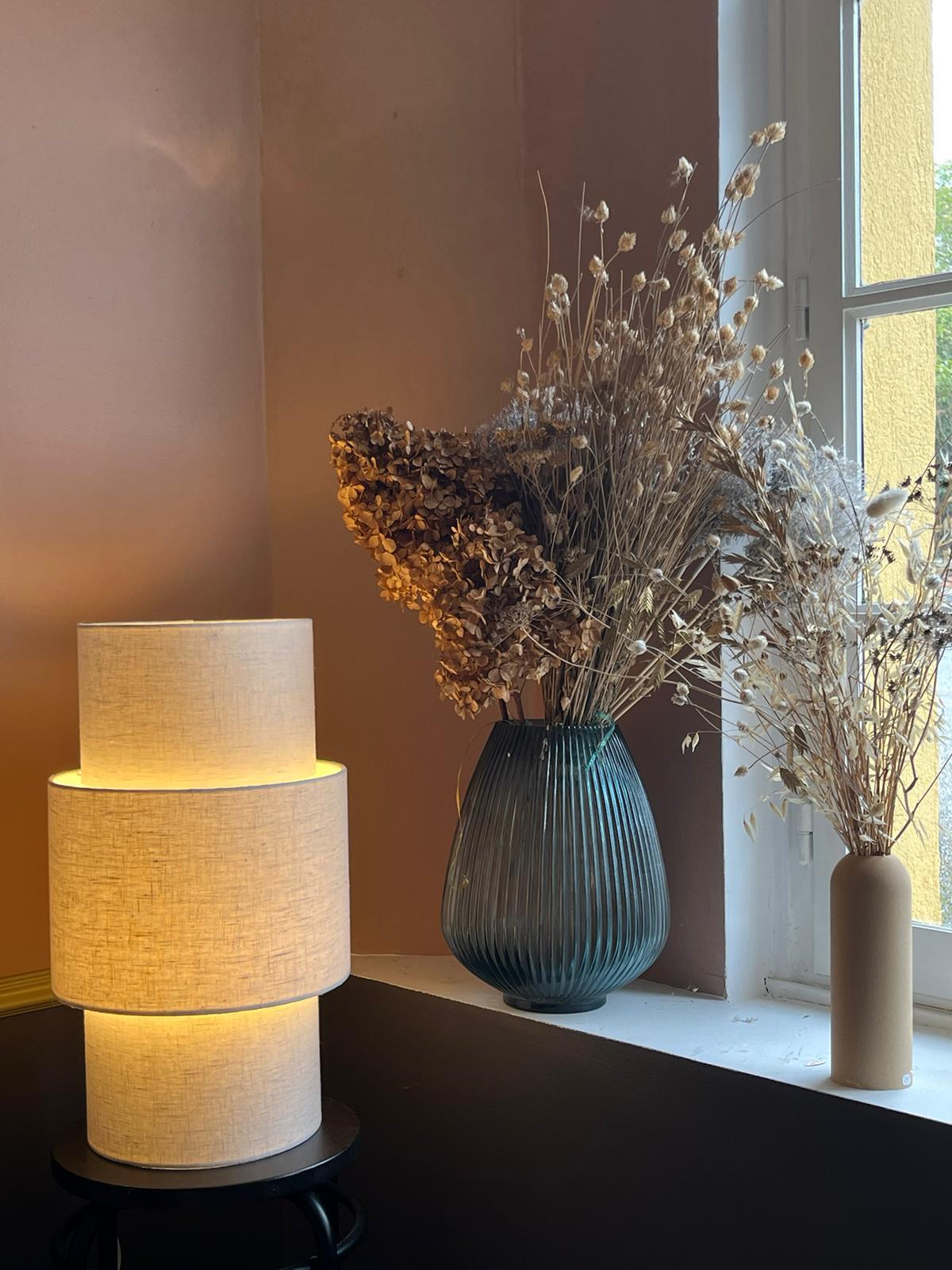 Lampe cylindrique claire posÃ©e prÃ¨s d'un vase bleu et de fleurs sÃ©chÃ©es