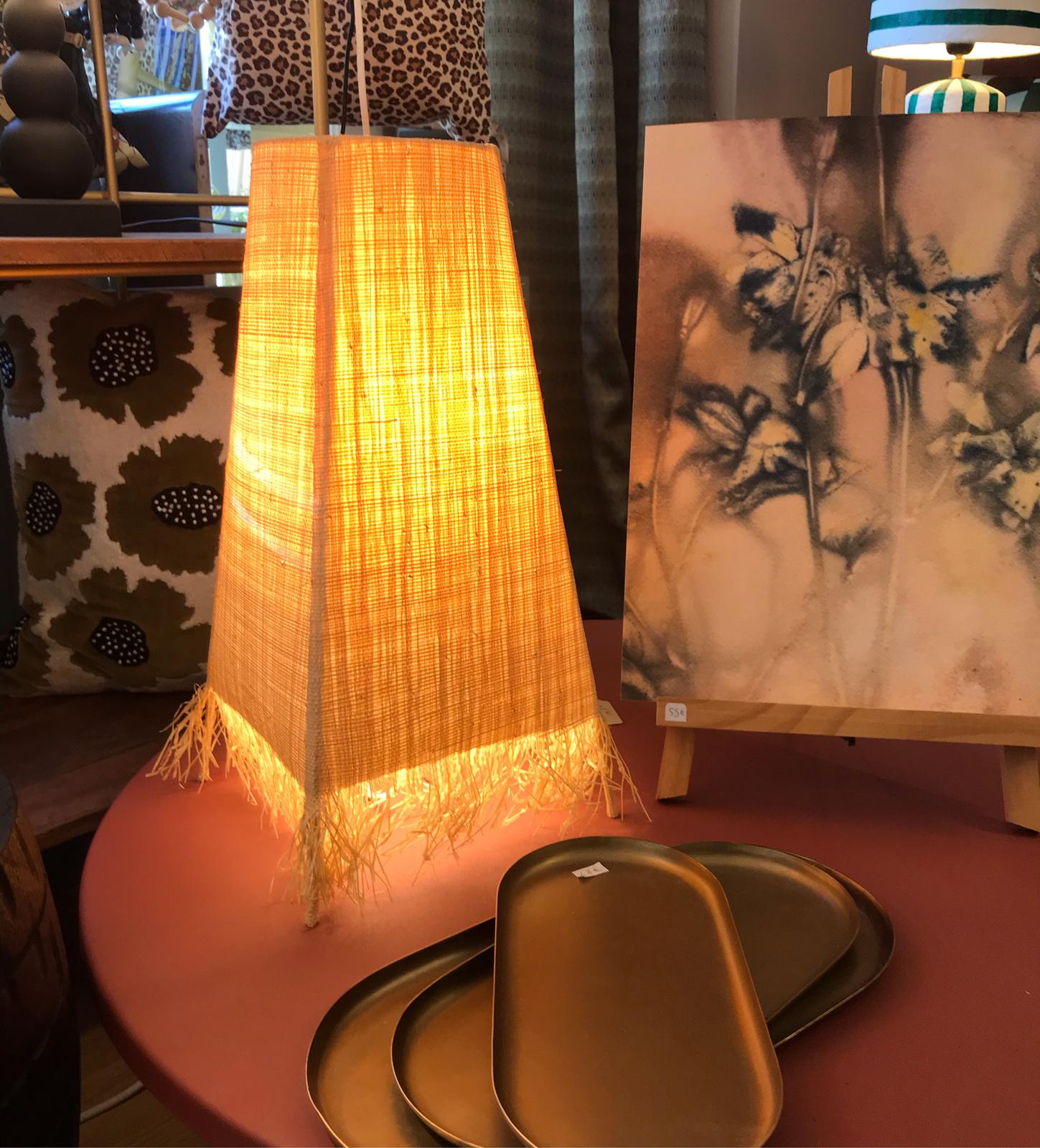 Lampe conique lumineuse avec franges posÃ©e sur une table rose Ã  cÃ´tÃ© d'une petite toile