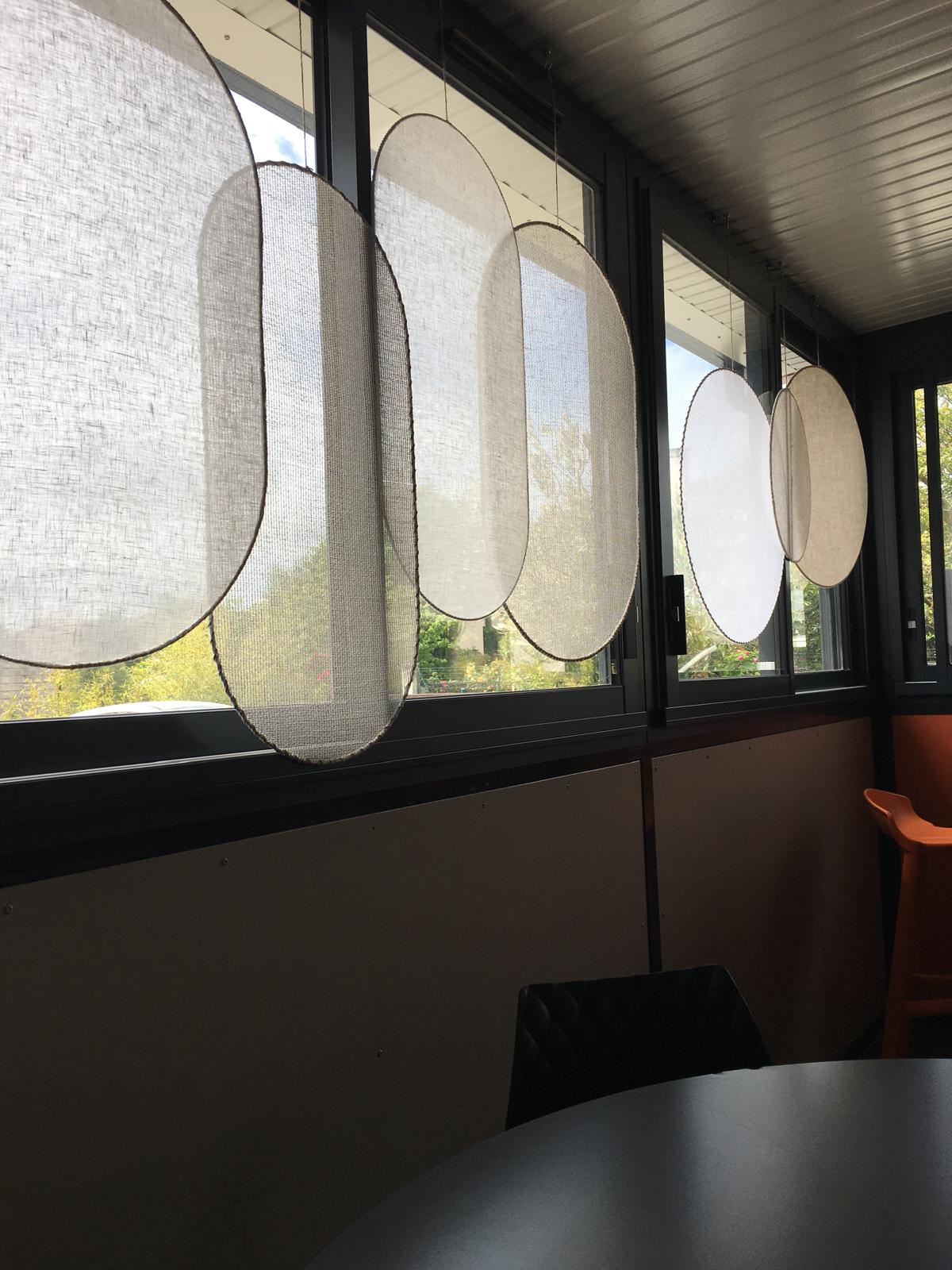 Installation de panneaux textiles ovales suspendus devant une série de fenêtres
