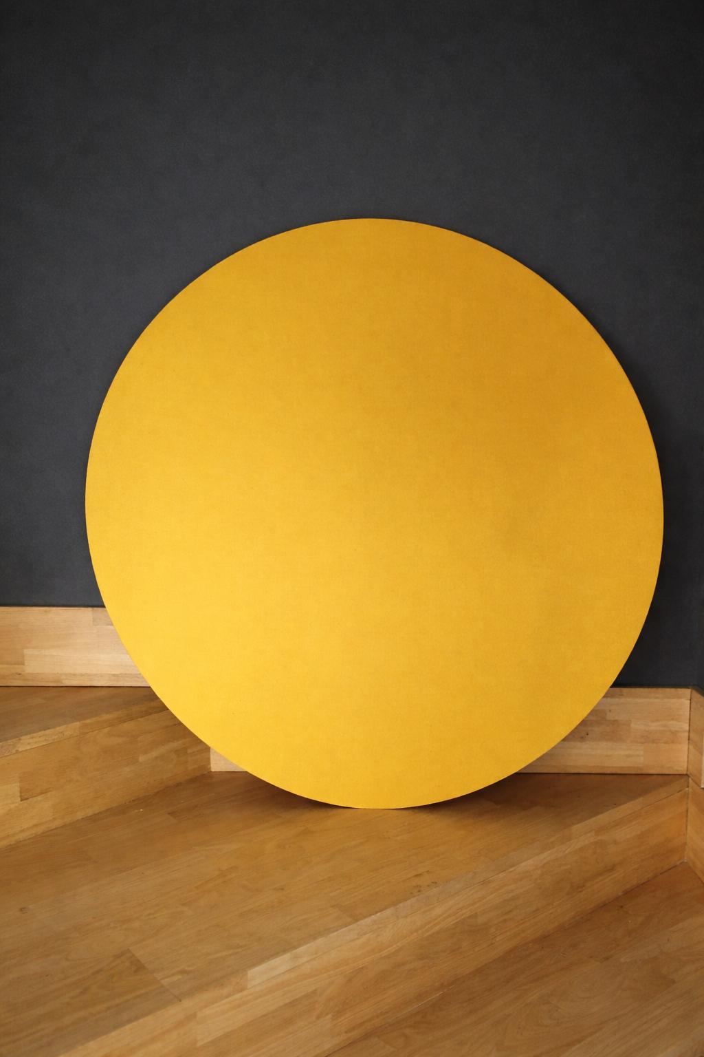 Grand tableau rond en tissu jaune posé contre un mur sombre
