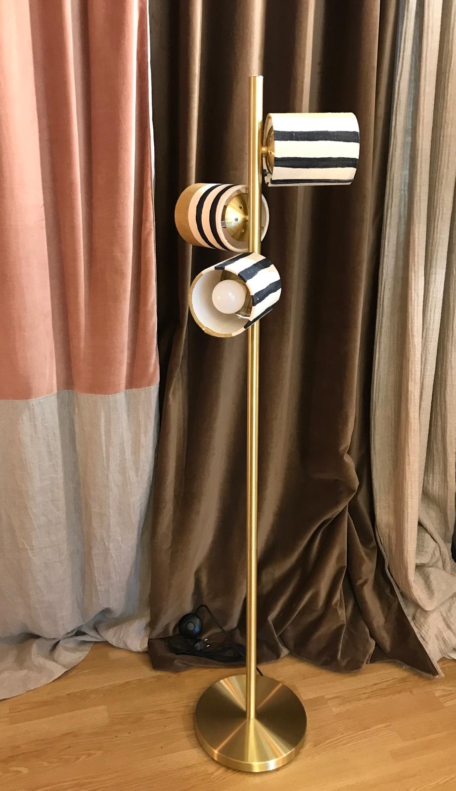 Lampadaire doré à trois têtes avec petits abat-jour rayés noir et blanc