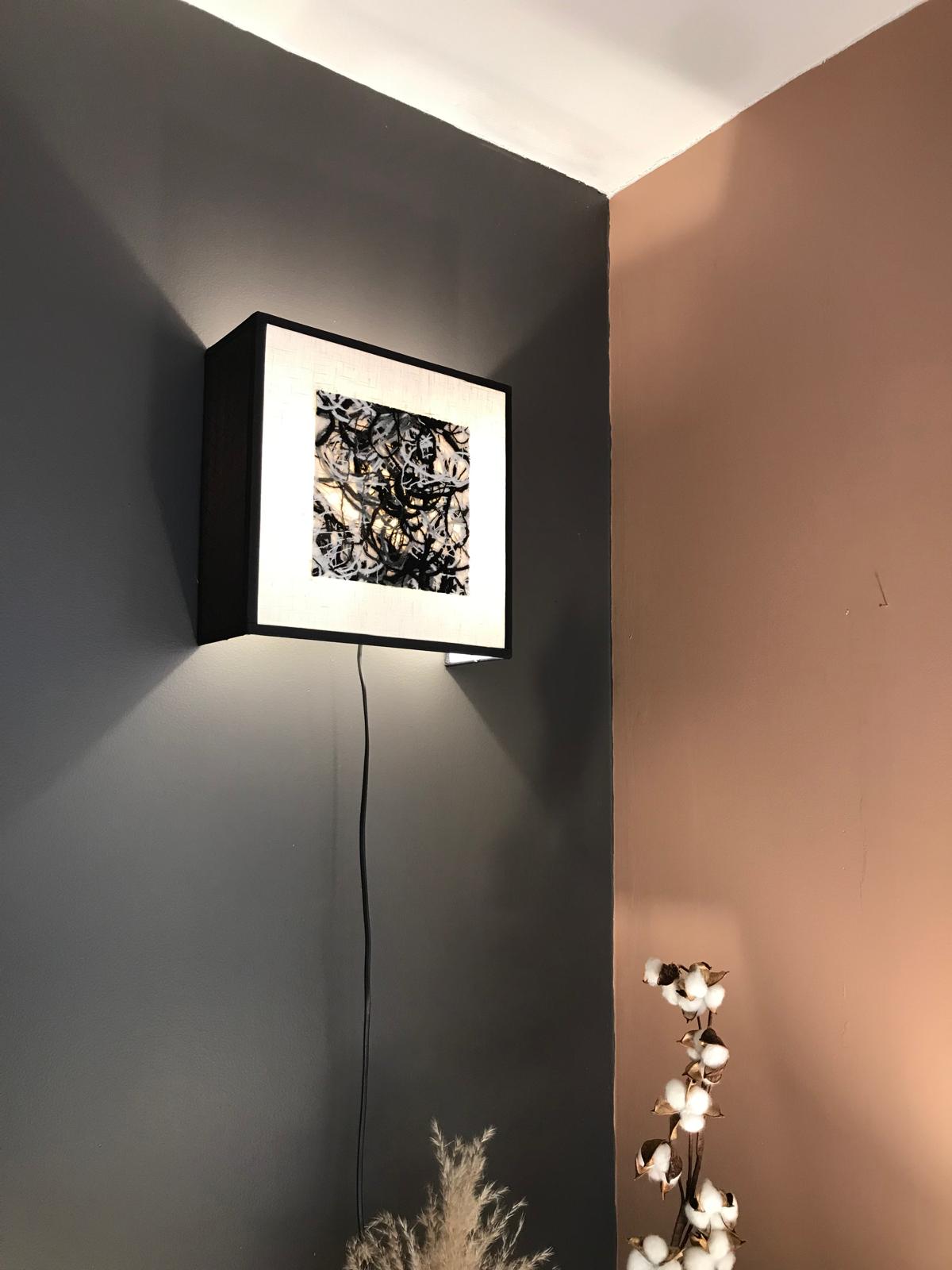 Applique carrée blanche et noire avec insert central abstrait, installée dans un angle